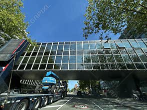 Modern glass pedestrian bridge above tree lined city street with construction