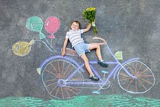 Little kid boy having fun with bicycle chalks picture on ground