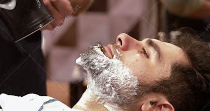 Man getting his beard shaved with shaving brush in barber shop
