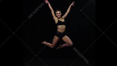 Acrobat girl jumps bending the knees. Slow motion. Black background