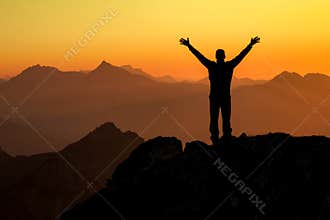 Happy success winning man on summit arms up at sunset
