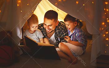 Happy family father and children reading a book in tent at hom