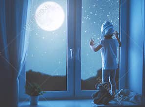 Child girl at window dreaming starry sky at bedtime
