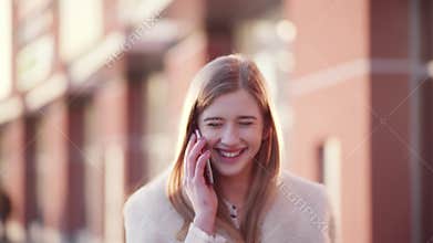 Young pretty business woman calling her friend using mobile phone and laughing while walking past a modern building.