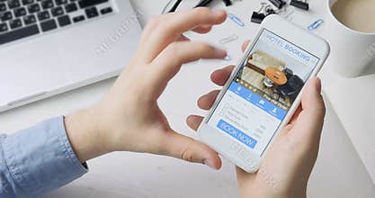 Man booking hotel suit using his smartphone and online booking mobile app sitting at his desk