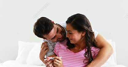 Happy couple looking at pregnancy test on bed in bedroom