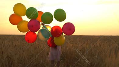 Young girl in the dress with colorful ballons is running across the field.