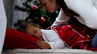 Mother comes and covers sleeps on floor baby with a red plaid at Christmas eve.
