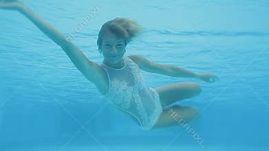 Happy beautiful woman swimming underwater in swimming pool. She smiles