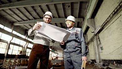 Professional designer and worker with level discovering new object on construction area. Chief and employee standing