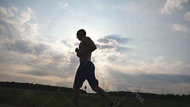 Silhouette of muscular man jogging in the country road at sunset. Male jogger training for marathon run outdoor. Athlete