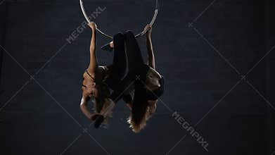 Graceful girls performs a gymnastic element on the aerial hoop