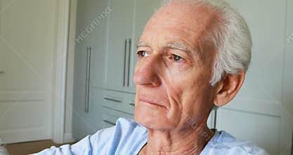 Senior man sitting in wheelchair looking through window in bedroom