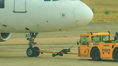 Tow tractor pushbacks airliner along airfield workers walk near