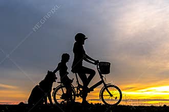 Silhouette biker lovely family at sunset over the ocean. Mom and daughter with dog bicycling at the beach.