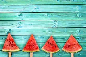 Four watermelon slice popsicles on blue wood background with copy space, summer fruit concept