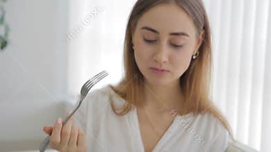 Young woman eating salad sitting on couch in apartment indoors.