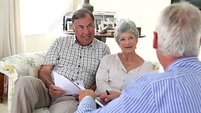 Senior Couple Sitting On Sofa Talking To Financial Advisor