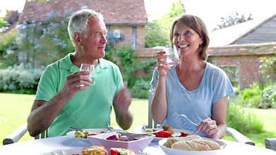 Senior Couple Sitting Outdoors Around Table Eating