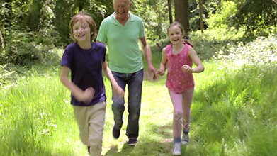 Grandfather Chasing Grandchildren Along Woodland Path