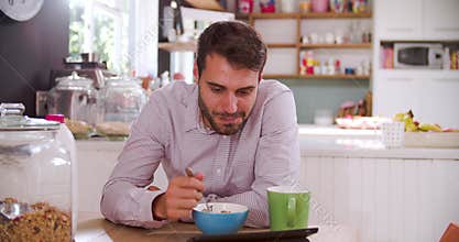 Young Man Eating Breakfast Whilst Using Digital Tablet
