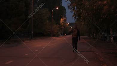 Man in summer night, with a backpack goes on road