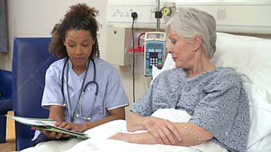 Nurse Sitting By Senior Female Patient's Bed In Hospital