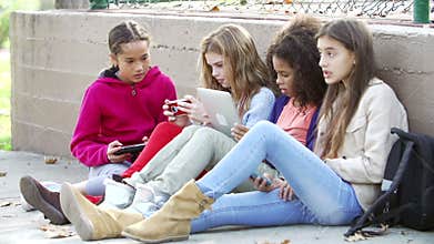 Young Girls Using Digital Tablets And Mobile Phones In Park