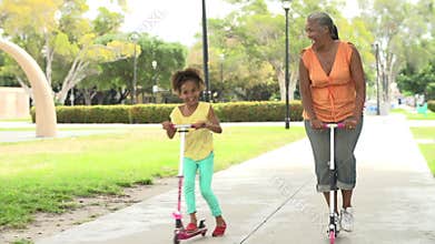 Grandmother And Granddaughter Riding Scooters In Park