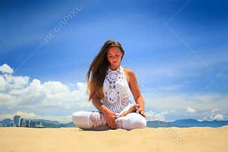girl in lace in yoga asana lotus on beach against blue sky