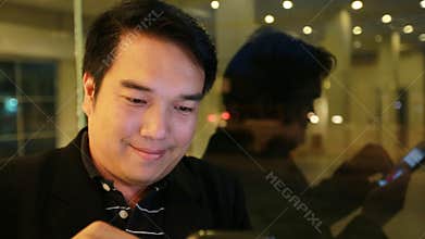 Asian business Man using on mobile phone and using smart phone at night in cafe. Handsome man waiting someone
