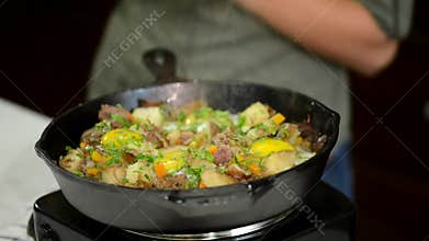 Woman adding green onion unto cast-iron frying pan.