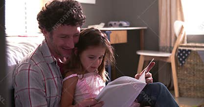 Father And Daughter Reading Book In Child's Bedroom