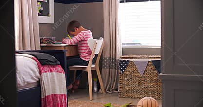 Boy Sitting At Desk In Bedroom Doing Homework