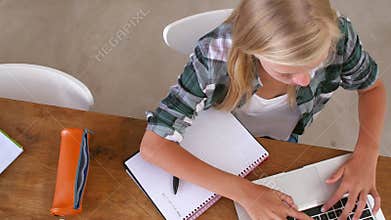 Overhead View Of Girl Doing Homework At Table On Laptop