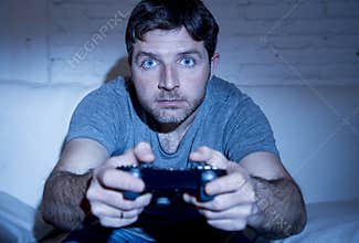 Young excited man at home sitting on living room sofa playing video games using remote control joystick