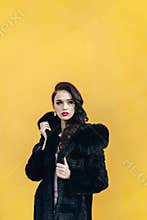 Beautiful girl in a black fur coat. Yellow background