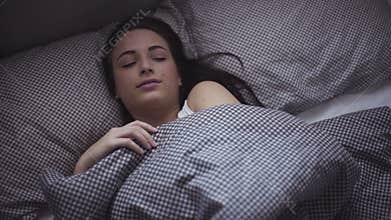 Female in her 20s wakes up in the morning in a bed, girl is stretching herself after sleeping.