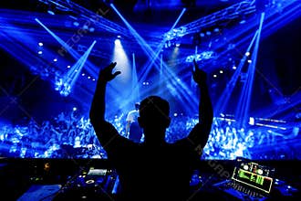DJ hands up at night club party under blue light with crowd of people