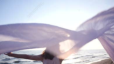 Beautiful woman holding light fabric on the beach and enjoy the sunset