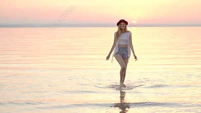 Young blonde woman in hat enjoying summer holidays on the ocean golden sunset