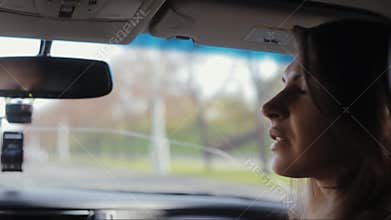 Pretty woman is sitting in a car. She looks in the window, turns her head and talks to the driver, Traveling by car.