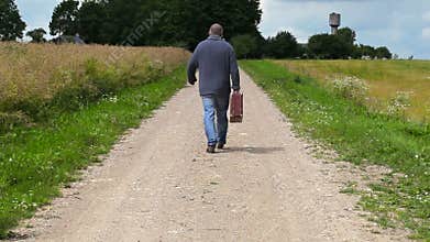 Man with suitcase walking away on rural road