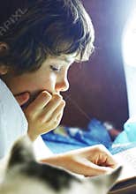 Boy read book in bed with cat