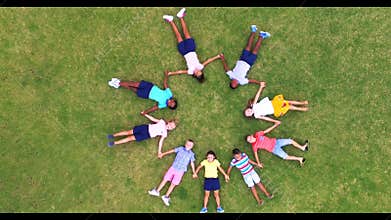 School kids holding hands while lying in circle on grass