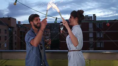 Couple having fun waving with firework candles and toasting with champagne