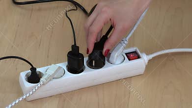 Female hands connect wire plugs to extension switch on wooden floor.
