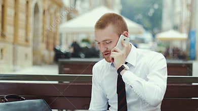Young businessman sitting at the bench working on agreement and talking on mobile phone