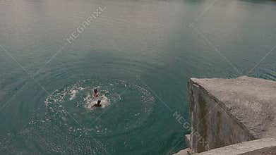 Teenager boy jumping off cliff to his friend into the water. Summer fun lifestyle