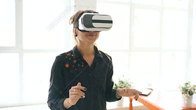 Woman in VR headset looking up and trying to touch objects in virtual reality at home indoors